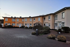 Ein mehrstöckiges Wohngebäude mit einem gepflasterten Innenhof, kleinen Sträuchern und wolkenlosem Himmel.