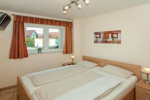 Ein Doppelbett mit zwei Nachttischen, ein Fenster mit Vorhängen, ein Gemälde an der Wand und eine Deckenleuchte.