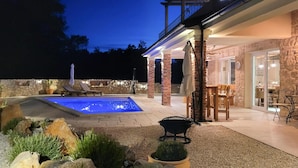 Ein Pool mit einer Steinterrasse, Sitzgelegenheiten im Freien und ein Steinhaus mit Balkon.