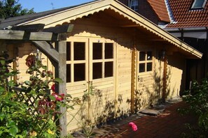 Eine Holzhütte mit Satteldach, einer Veranda mit Geländer und einem Fenster mit Rollo.