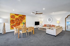 Ein modernes Wohnzimmer mit Essbereich, Deckenventilator, Flachbildfernseher und einem großen Gemälde mit Tomaten.