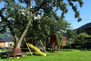 Ein Spielplatz mit Rutsche, Schaukeln und einem roten Spielhäuschen.