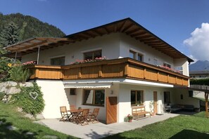 Eine zweistöckige Chalet mit Holzbalkon, einer Terrasse mit Gartenmöbeln und einem Blick auf die Berge.