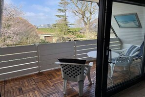 Ein Balkon mit Holzboden, einem weißen Stuhl und einem Tisch mit Sitzkissen.