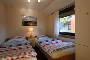 Ein Schlafzimmer mit zwei Betten, einem Nachttisch, einer Lampe, einem Bild an der Wand und einem Fenster mit Vorhängen.