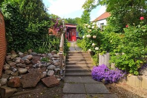 A garden pathway leading to a red door, surrounded by lush greenery and flowering plants. - Holiday home in KARBY with swimming pool (KARBY)