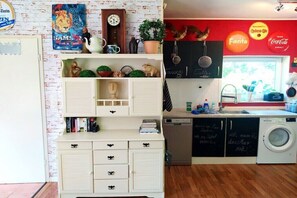 A kitchen with a sink, dishwasher, and a washing machine. There are shelves with various items and a clock on the wall. - Holiday home in KARBY with swimming pool (KARBY)