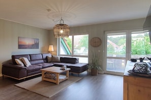 Ein Wohnzimmer mit Sofa, Couchtisch, Lampe und großen Fenstern.