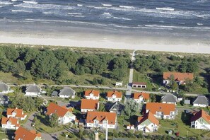 Luftaufnahme einer Küstenwohngegend mit Häusern, einem Strand und einem bewaldeten Hügel.