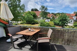 Ein Balkon mit Tisch und Stühlen, ein Korbstuhl und Blick auf Häuser und Grünflächen.