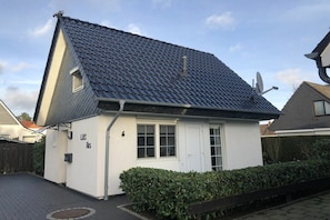 Ein kleines, eingeschossiges Haus mit einem dunklen Ziegeldach, einer weißen Fassade und einem kleinen Fenster.