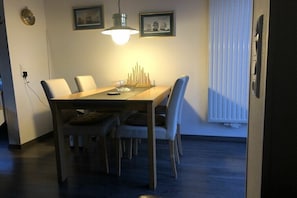 Ein Essbereich mit einem Holztisch, weißen Stühlen, einer Hängeleuchte und gerahmten Bildern an der Wand.