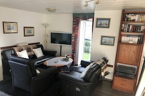 Ein Wohnzimmer mit einer Sofagarnitur, einem Flachbildfernseher, einem Couchtisch mit einer Vase und einem Bücherregal.