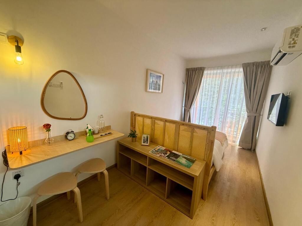 Une pièce avec un banc en bois, une petite table avec une lampe, un miroir et une fenêtre avec des rideaux.