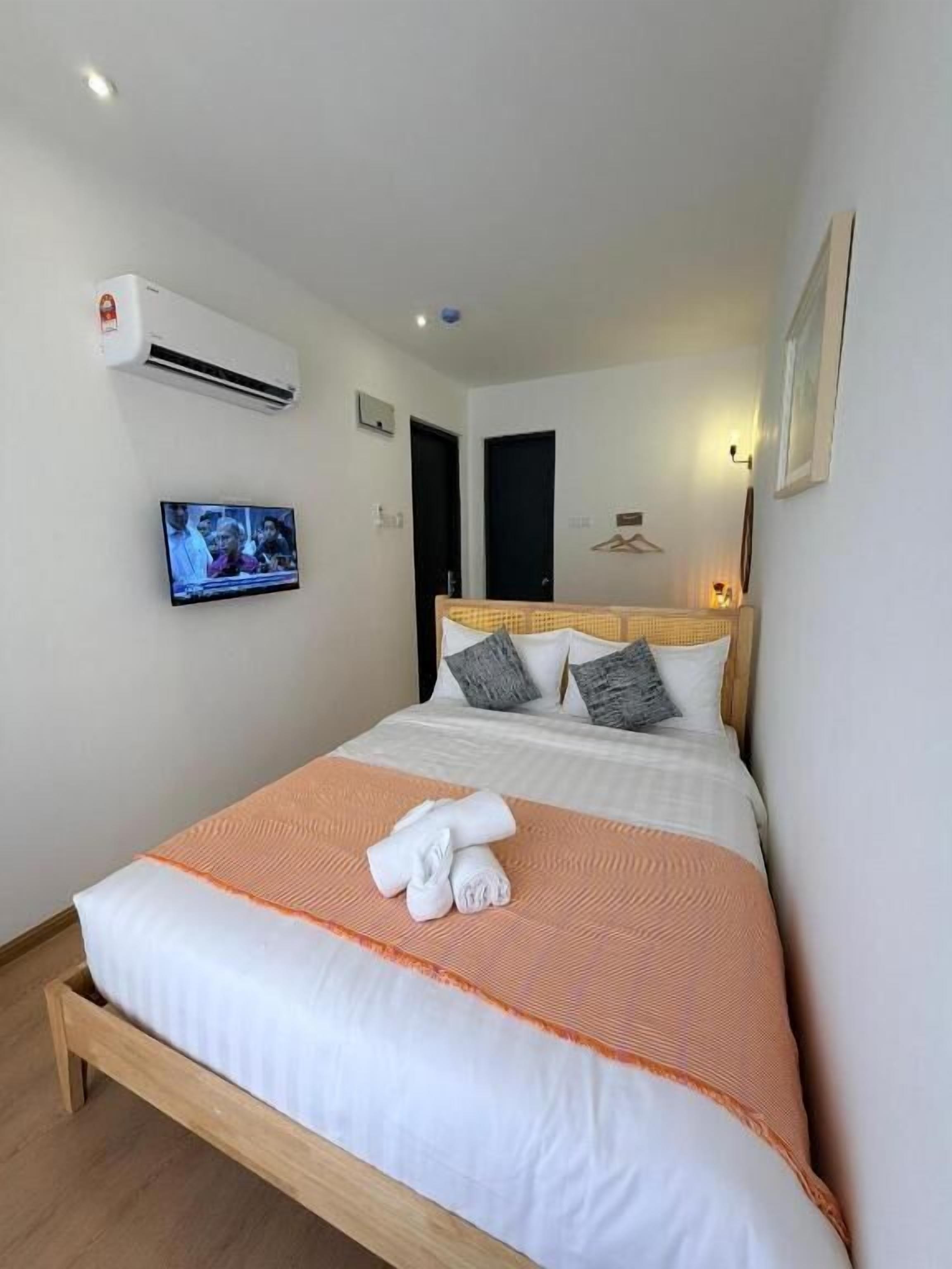 A hotel room with a bed, a television, an air conditioning unit, and a door.