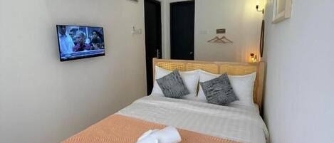 A hotel room with a bed, a television, an air conditioning unit, and a door.