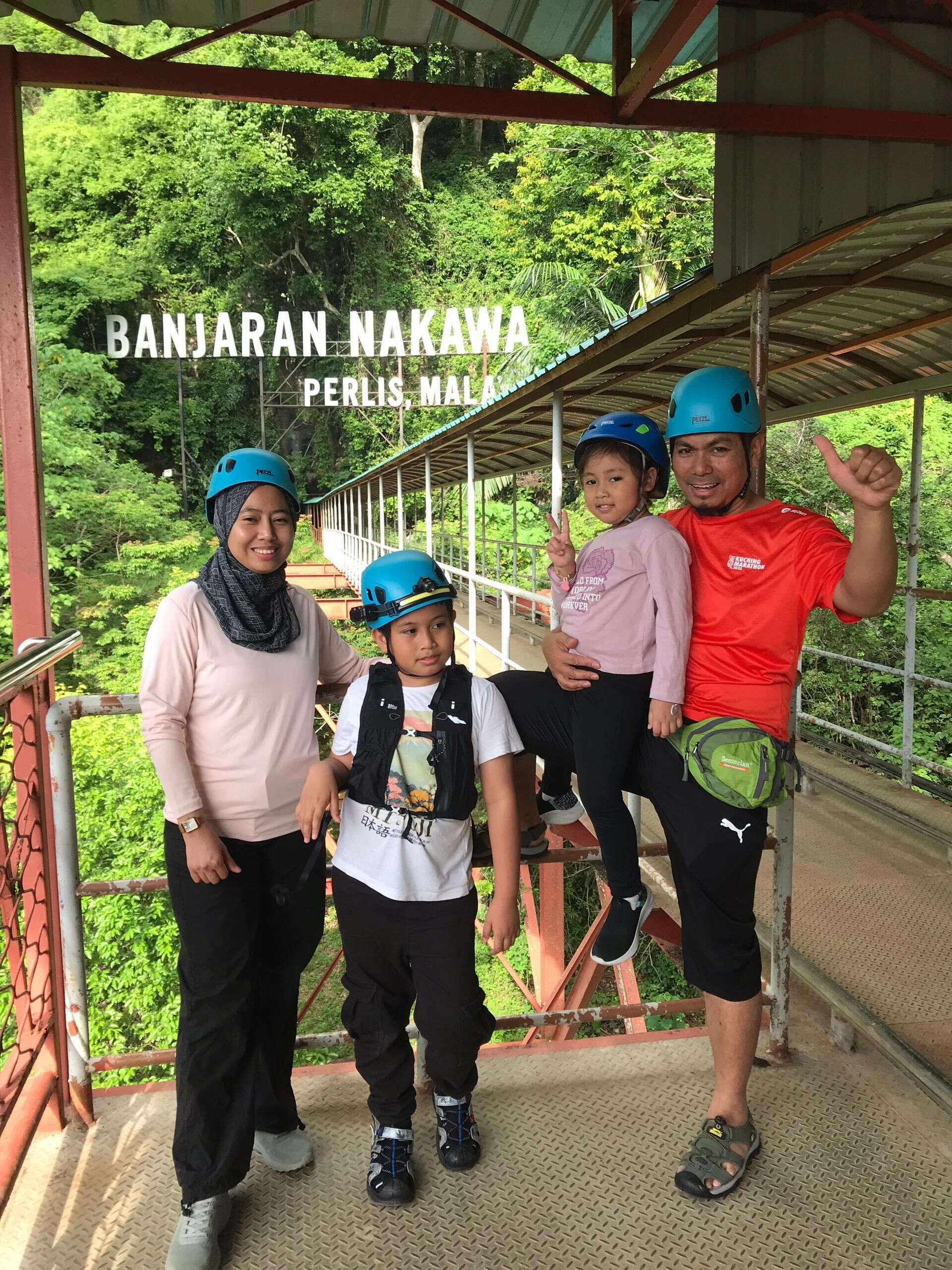 A group of people wearing helmets and standing on a bridge with a metal railing, surrounded by greenery.