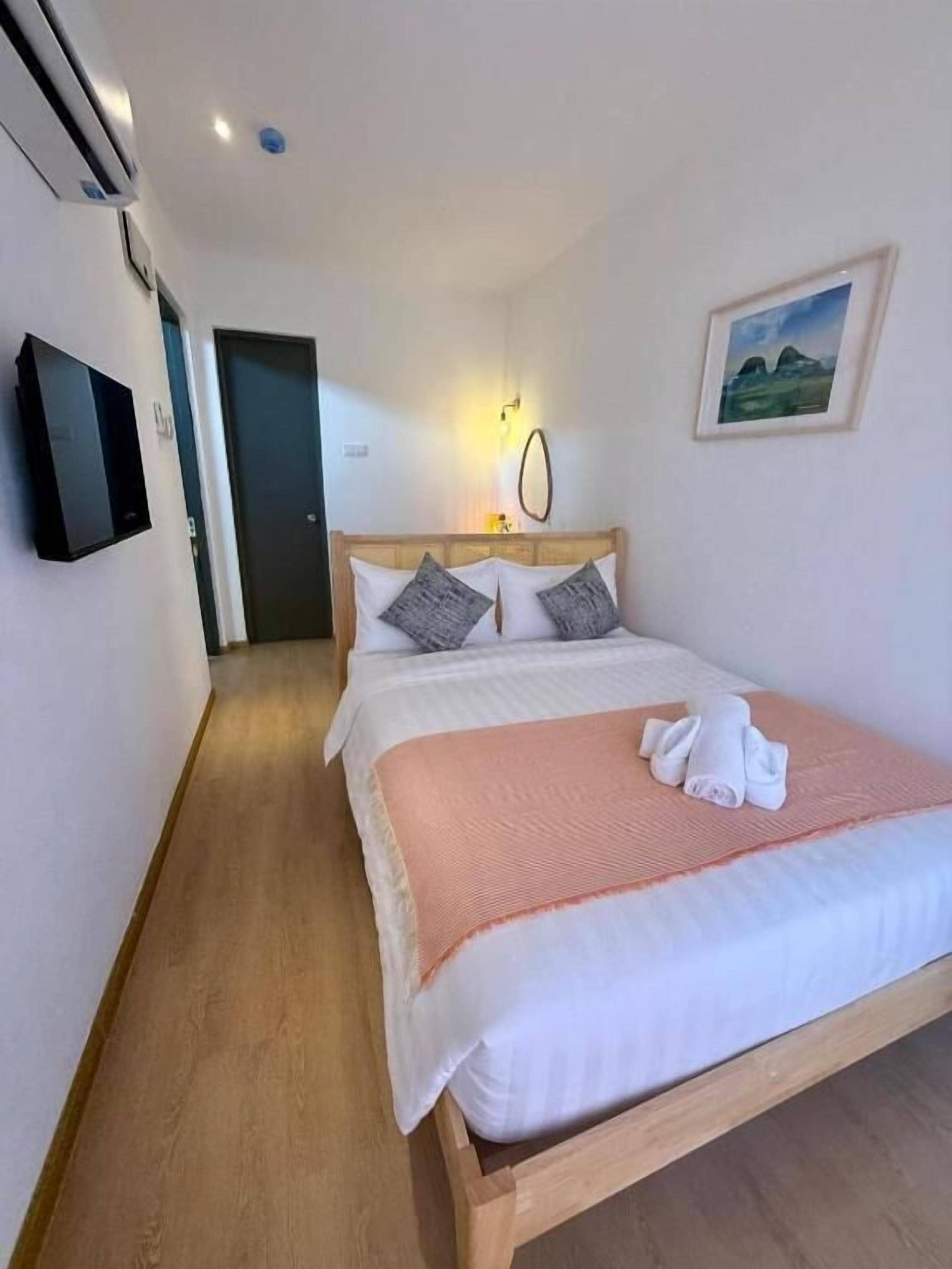 A hotel room with a wooden bed, a television, a framed picture on the wall, and a door leading to another room.