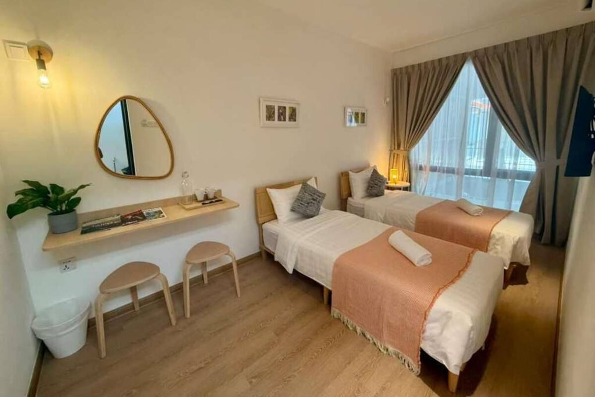 Ein Hotelzimmer mit zwei Betten, einer kleinen Sitzecke, einem Spiegel und einem fenster mit Vorhängen.
