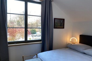 A bedroom with a bed, a bedside table with a lamp, a window with curtains, and a framed picture on the wall. - Holiday home with 2 bedrooms (Kurort Gohrisch OT Papstdorf)
