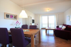 Ein modernes Wohnzimmer mit einem Holzesstisch, violetten Stühlen, einem roten Sofa und einem großen Fenster.