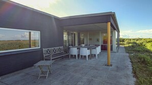 Une terrasse extérieure moderne, dotée d’une table et de chaises, d’un banc et offrant une vue sur le paysage.