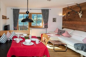 Ein gemütlicher Essbereich mit rotem Tischlein, Holzmöbeln und Blick ins Freie durch ein Fenster.
