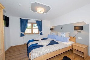 Ein Schlafzimmer mit einem Bett, einem Nachttisch, einer Wandlampe, einem an der Wand befestigten Fernseher und einem Fenster mit Vorhängen.