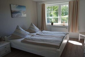 Ein Schlafzimmer mit Bett, Nachttisch, Fenster mit Vorhängen und einem Gemälde an der Wand.