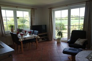 Ein Essbereich mit Tisch, Stühlen, einem Fernseher und Blick ins Freie.