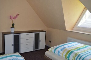 Une chambre à coucher avec un lit, une commode, une fenêtre avec des stores et un pot d’orchidée.