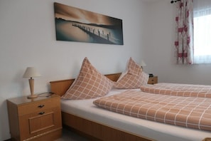 Ein Doppelbett mit karierter Bettdecke, ein Nachttisch mit Lampe, eine Schublade und ein Bild eines Piers an der Wand.
