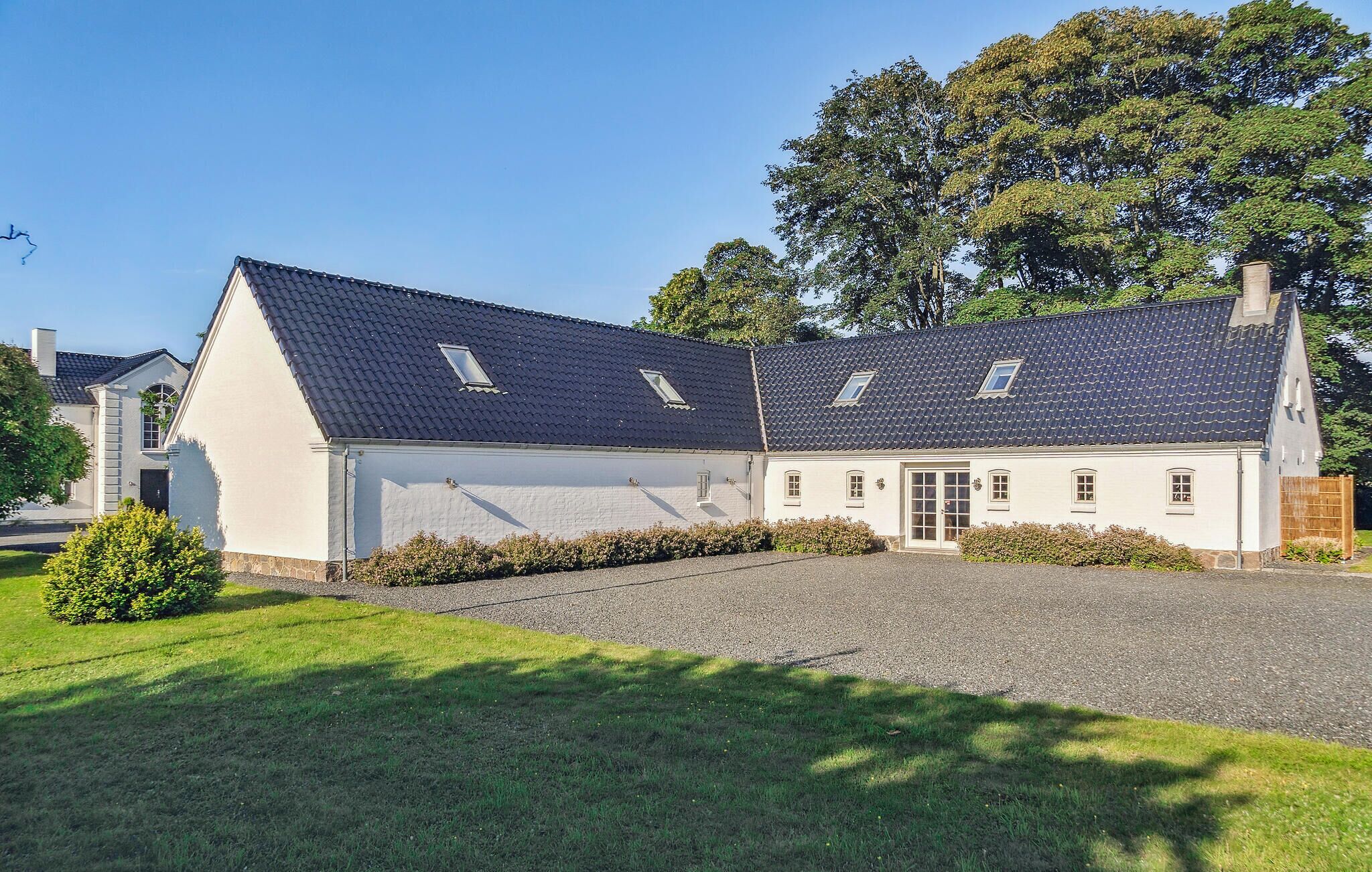 A two-story white building with a dark tiled roof, a central entrance, and a gravel driveway.