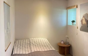 Un dormitorio con cama, una mesita de noche de madera, una planta en maceta y una ventana con vistas.