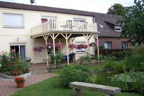 Ein zweigeschossiges Haus mit einem Balkon, einem Garten voller Blumen und einem Teich.