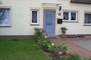 Ein Haus mit einer blauen Tür, Hausnummer 22, und einem kleinen Garten mit Blumen.