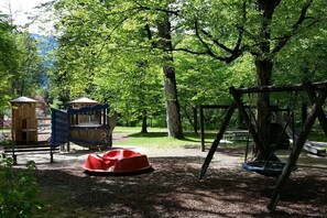 A playground with a swing set, a red slide, and a wooden playhouse. - Schmittenblick - Haus Hollaus (Zell am See)