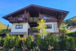 A two-story chalet with a sloped roof, balconies with plants, and a garden in front. - Schmittenblick - Haus Hollaus (Zell am See)