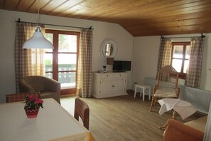 Ein gemütliches Zimmer mit Esstisch, Stühlen, einem weißen Schrank, einem Fernseher und einem Korbstuhl.
