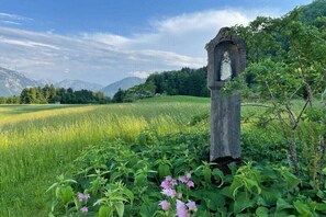 Ein Steinbauwerk mit einer Statue, umgeben von üppigem Grün und Bergen im Hintergrund.