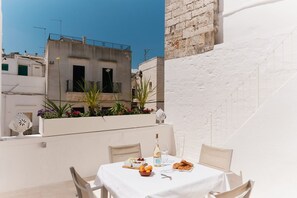 Eine Dachterrasse mit Esstisch, einer Weinflasche und Blick auf umliegende Gebäude.