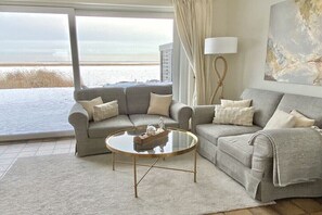 A living room with two grey sofas, a glass coffee table, a lamp, and a large window with a view of the sea. - Holiday home with 3 bedrooms (Sylt, OT Rantum)