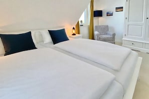 A double bed with white bedding, a bedside table with a lamp, a checkered chair, and a wardrobe. - Holiday home with 3 bedrooms (Sylt, OT Rantum)