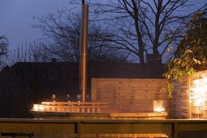 Eine Holzterrasse mit Metallkonstruktion, möglicherweise einem Grill, und einer Ziegelwand.