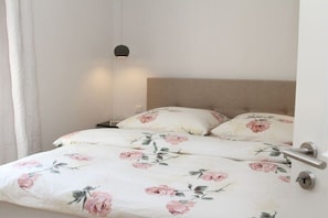 Un lit avec une literie à motifs floraux, une table de chevet et un luminaire suspendu.
