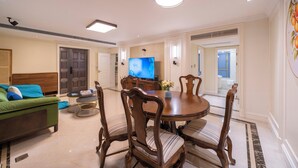Una sala de estar moderna con un sofá verde, una mesa de comedor de madera y sillas, un televisor de pantalla plana y un jarrón decorativo.
