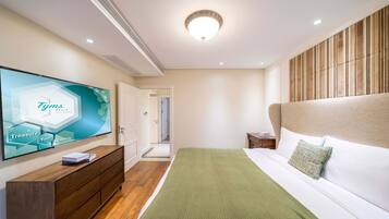 Una habitación de hotel moderna con una televisión de pantalla plana grande, un tocador de madera, una cama con una manta verde y un cabecero de madera.