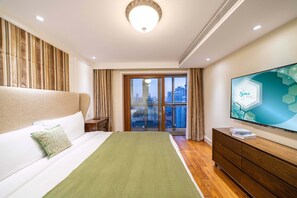 Ett hotellrum med en säng, en tv, en byrå i trä och utsikt över staden genom fönstret.