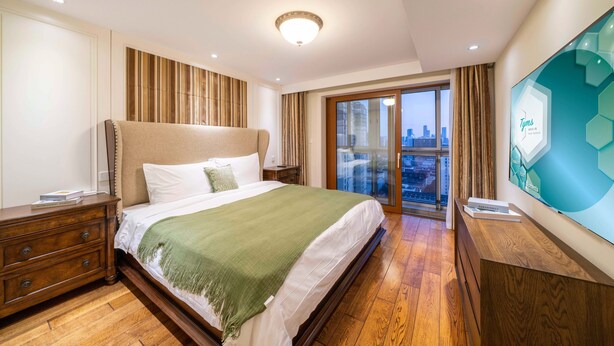 Habitación de hotel con una cama grande, un aparador de madera, un televisor y un balcón con vistas a la ciudad.