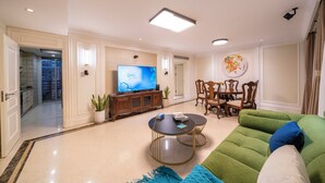 Una sala de estar moderna con televisor de pantalla plana, un sofá verde, una mesa de comedor con sillas y una planta en maceta.